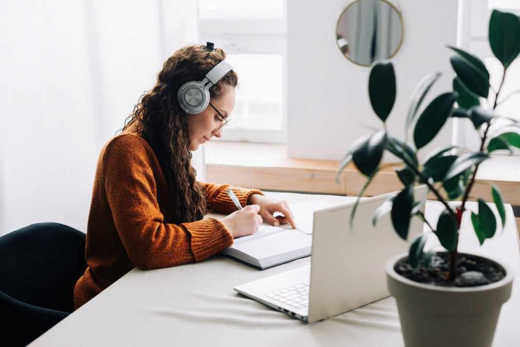 Estudiante con audífonos toma un curso en línea desde su computador portátil