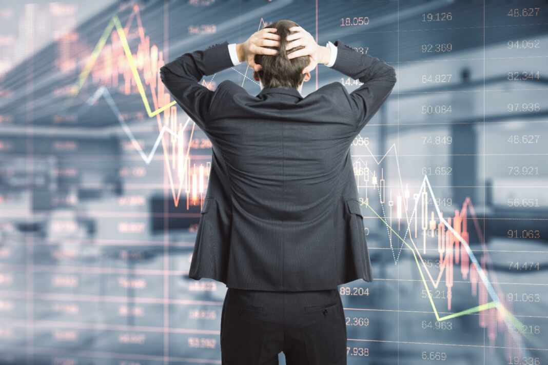 Operador de bolsa frente a pantallas con gráficos financieros en descenso