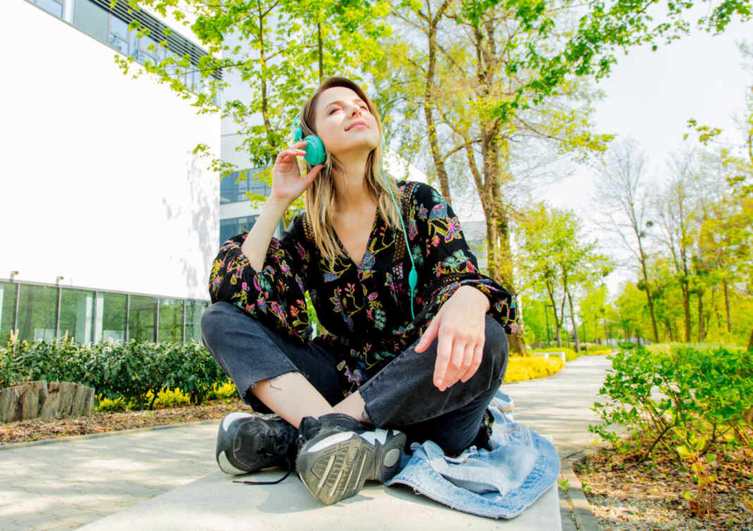 Mujer joven escuchando música con auriculares sentada al aire libre