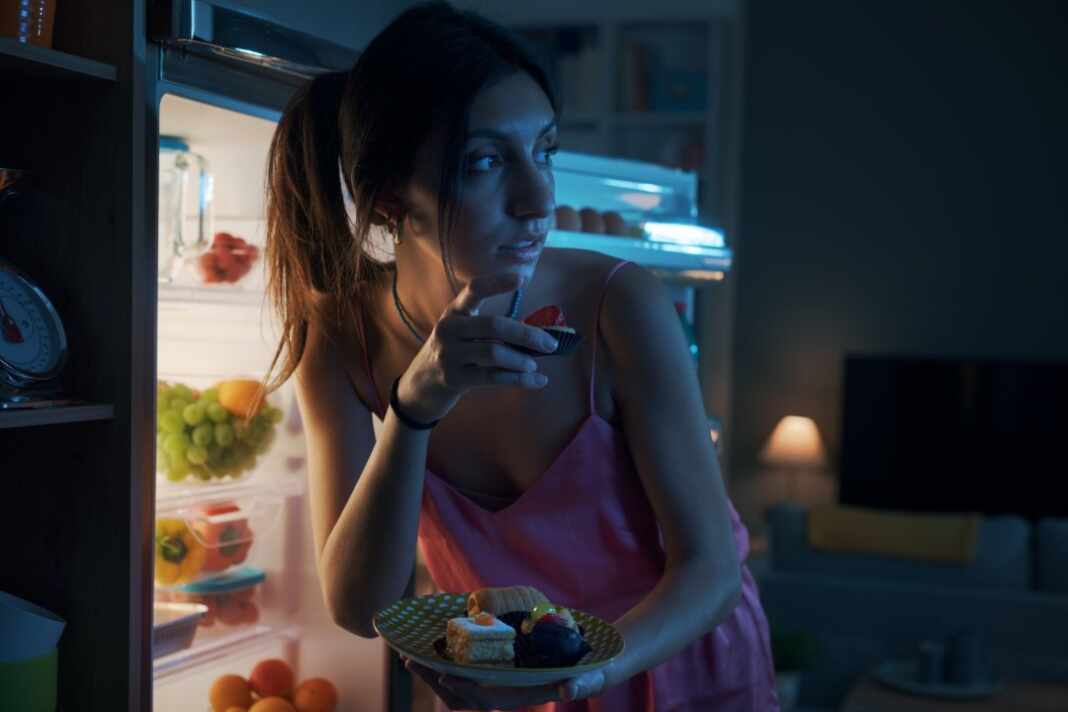 Persona que abre el refrigerador para comer de noche en una cocina a oscuras