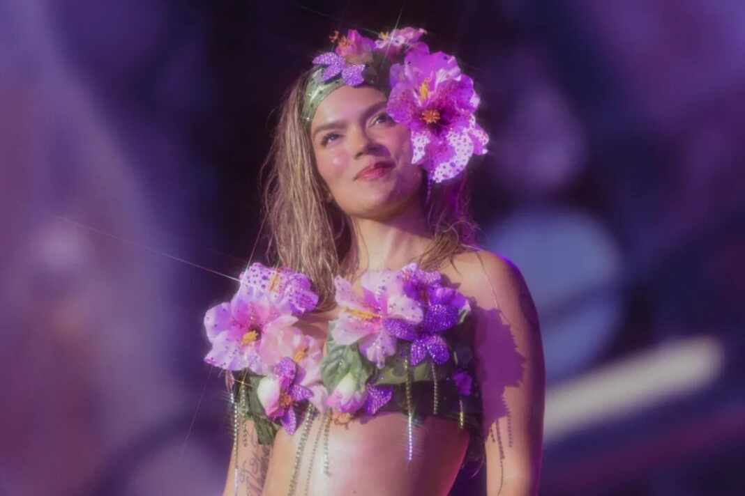 Karol G en concierto con flores moradas en el cabello durante su gira