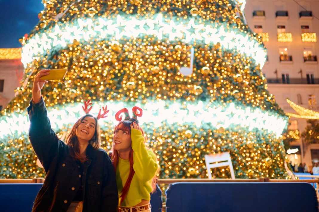 Amigas se toman una selfie frente a un árbol de Navidad iluminado, época en que buscan cuidar casas en Japón